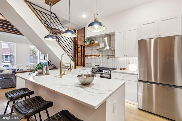 kitchen featuring white cabinetry, light stone countertops, wall chimney range hood, light hardwood / wood-style floors, and appliances with stainless steel finishes