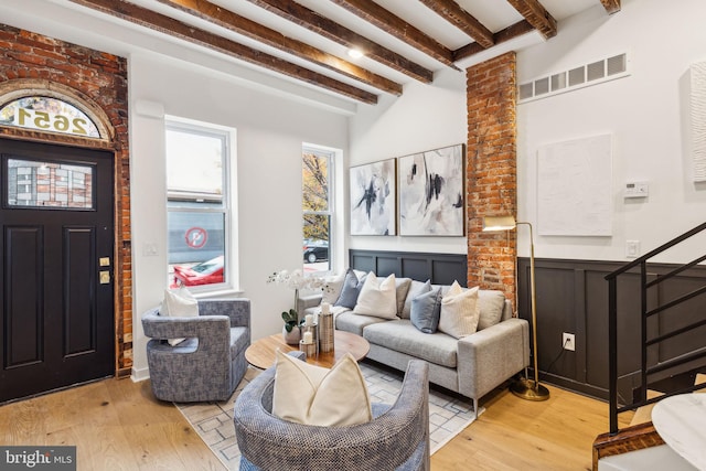 living room with beam ceiling, light hardwood / wood-style floors, and brick wall