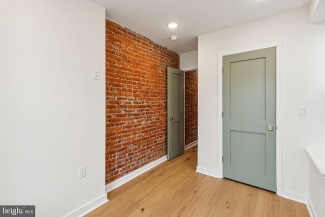 unfurnished room with light wood-type flooring and brick wall