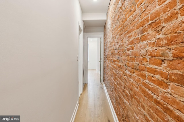 corridor with light hardwood / wood-style flooring and brick wall