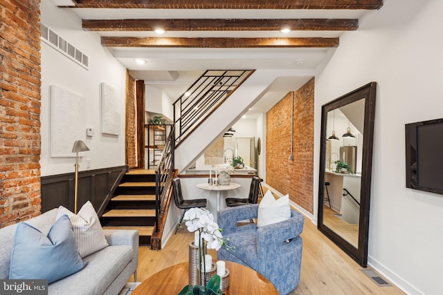 living room with beam ceiling, light wood-type flooring, and brick wall