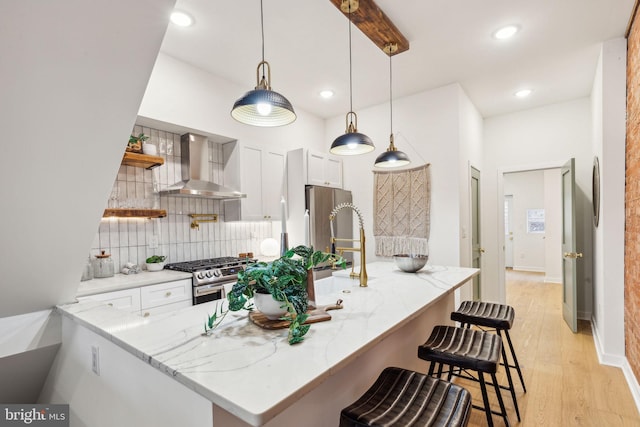 kitchen with kitchen peninsula, hanging light fixtures, wall chimney exhaust hood, white cabinetry, and stainless steel appliances