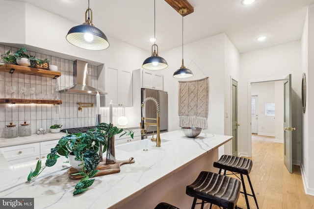 kitchen featuring light stone counters, white cabinetry, hanging light fixtures, and wall chimney range hood