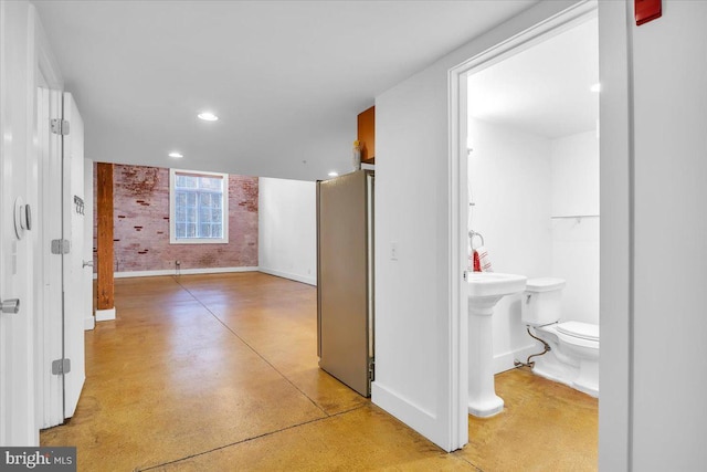 corridor with baseboards, recessed lighting, a sink, and finished concrete floors