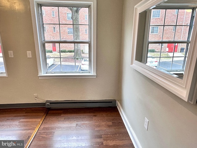 unfurnished room featuring a healthy amount of sunlight, dark hardwood / wood-style flooring, and baseboard heating