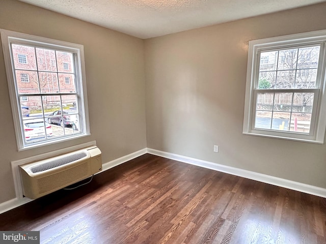 empty room featuring dark wood-type flooring, a wall mounted air conditioner, and a textured ceiling