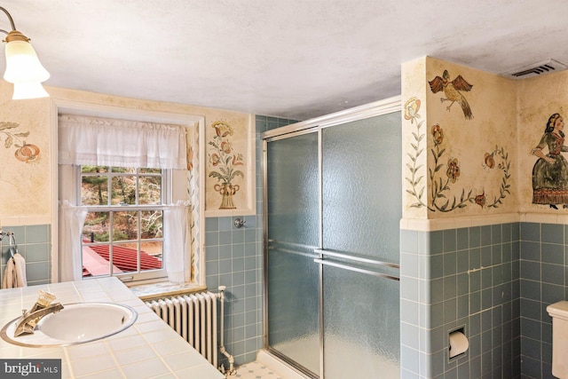 bathroom featuring radiator, sink, an enclosed shower, and tile walls