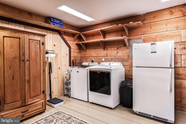 laundry area featuring light wood-type flooring, separate washer and dryer, and wooden walls