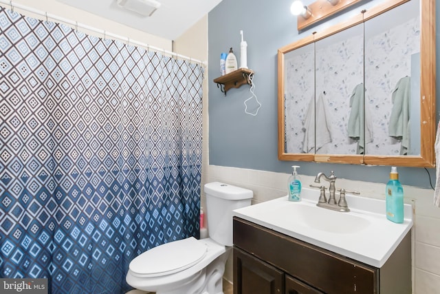 bathroom featuring walk in shower, vanity, tile walls, and toilet