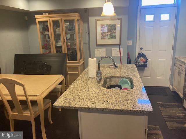 kitchen featuring a kitchen bar, light stone counters, sink, pendant lighting, and a center island with sink