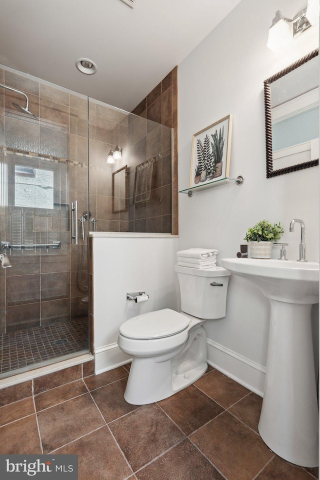 bathroom with toilet, tile patterned flooring, and tiled shower