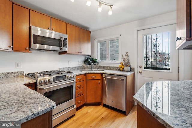 kitchen with light stone counters, sink, stainless steel appliances, and light wood-type flooring