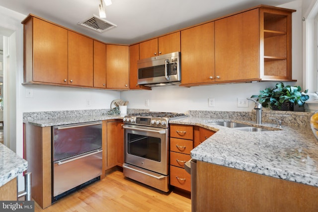 kitchen with light stone counters, light wood-type flooring, sink, and appliances with stainless steel finishes