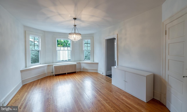 unfurnished dining area with light hardwood / wood-style flooring, an inviting chandelier, and radiator