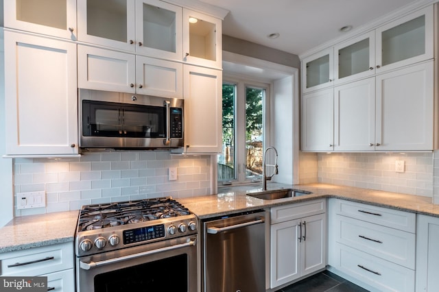 kitchen featuring sink, decorative backsplash, appliances with stainless steel finishes, light stone counters, and white cabinetry