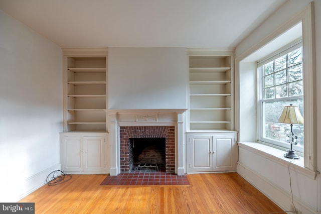 unfurnished living room with a fireplace, built in features, light hardwood / wood-style floors, and plenty of natural light