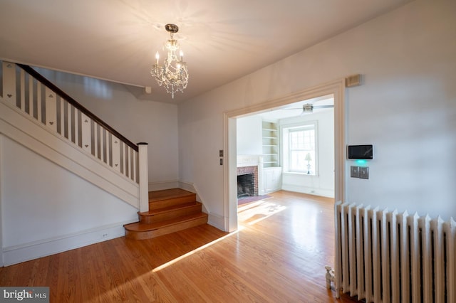 stairway featuring hardwood / wood-style flooring, built in features, a notable chandelier, a fireplace, and radiator heating unit