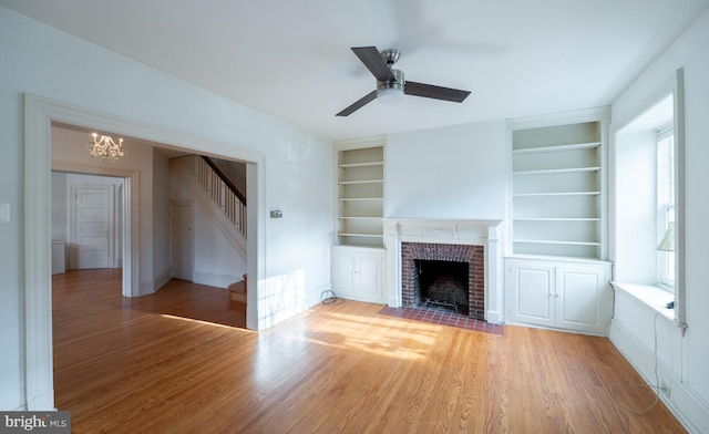 unfurnished living room featuring hardwood / wood-style flooring, built in shelves, a fireplace, and ceiling fan with notable chandelier