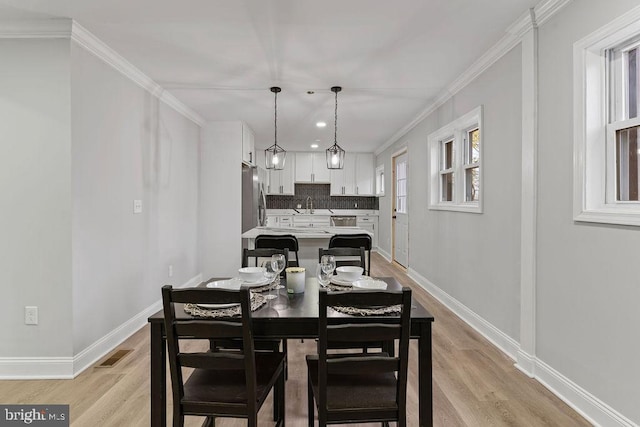 dining space with light wood-type flooring, plenty of natural light, crown molding, and sink