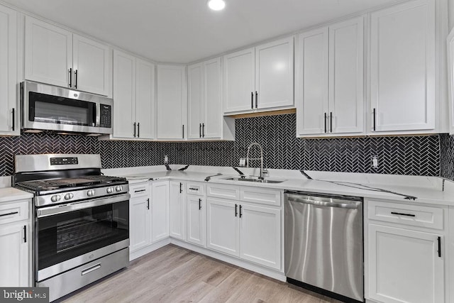 kitchen with white cabinets, sink, light hardwood / wood-style flooring, appliances with stainless steel finishes, and light stone counters