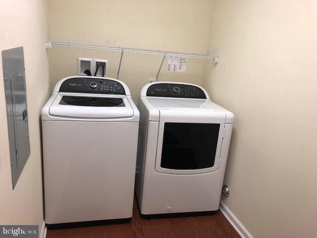 clothes washing area with washing machine and dryer, electric panel, and dark wood-type flooring