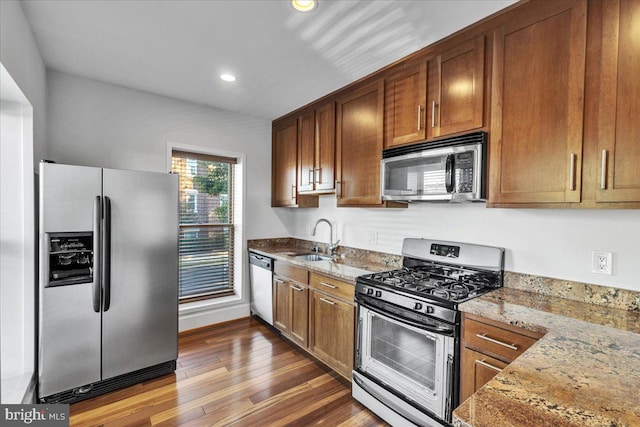 kitchen featuring dark wood-type flooring, appliances with stainless steel finishes, light stone countertops, and sink