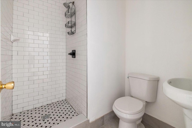 bathroom with a tile shower, sink, and toilet