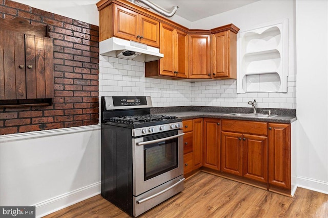 kitchen featuring light wood-type flooring, tasteful backsplash, stainless steel range with gas cooktop, and sink