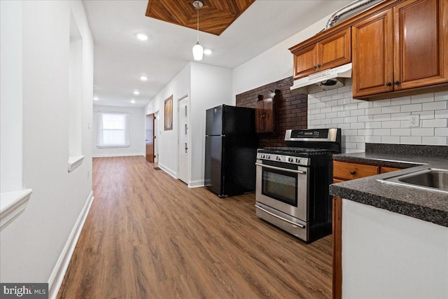 kitchen with black refrigerator, backsplash, stainless steel gas range, wood-type flooring, and hanging light fixtures