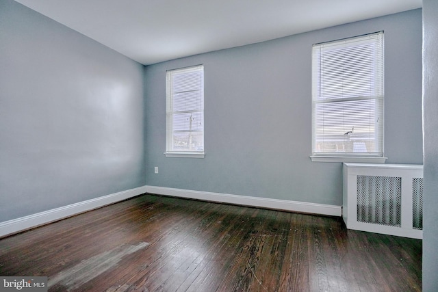 empty room featuring radiator, a wealth of natural light, and dark hardwood / wood-style flooring