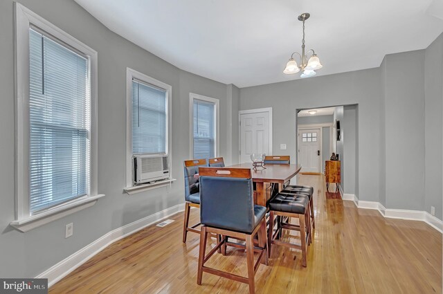 dining area with cooling unit, a notable chandelier, and light wood-type flooring