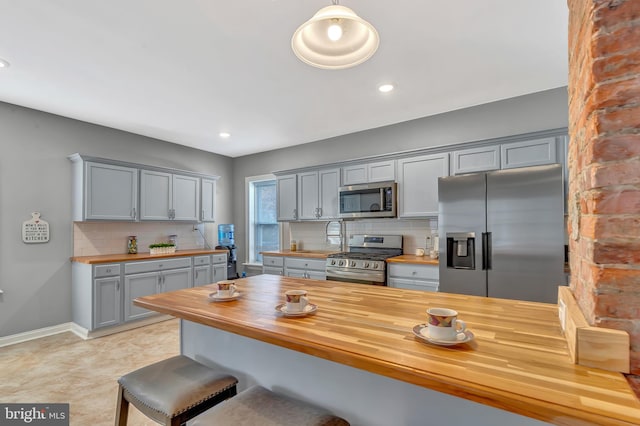 kitchen featuring stainless steel appliances, gray cabinetry, decorative backsplash, and wooden counters