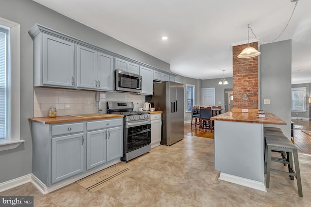 kitchen with stainless steel appliances, wooden counters, decorative light fixtures, a breakfast bar area, and light wood-type flooring