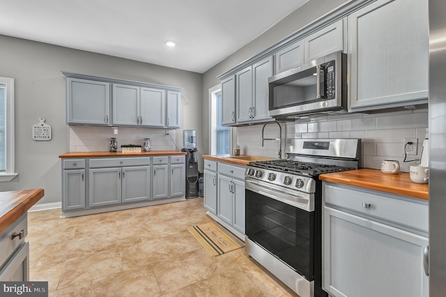 kitchen featuring gray cabinetry, wood counters, decorative backsplash, and appliances with stainless steel finishes