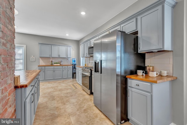 kitchen with gray cabinetry, wooden counters, light tile patterned floors, appliances with stainless steel finishes, and tasteful backsplash