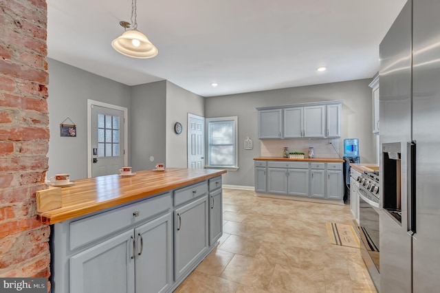 kitchen with pendant lighting, backsplash, gray cabinets, butcher block counters, and stainless steel appliances