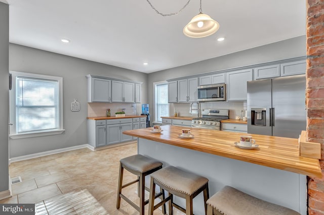 kitchen featuring backsplash, hanging light fixtures, gray cabinets, butcher block countertops, and stainless steel appliances