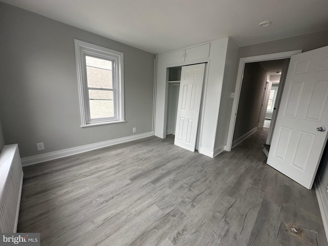 unfurnished bedroom with wood-type flooring, radiator, and a closet