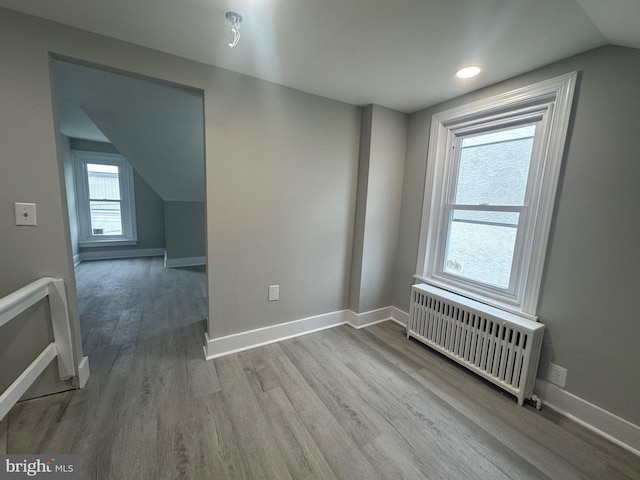 additional living space with light wood-type flooring, radiator heating unit, and vaulted ceiling