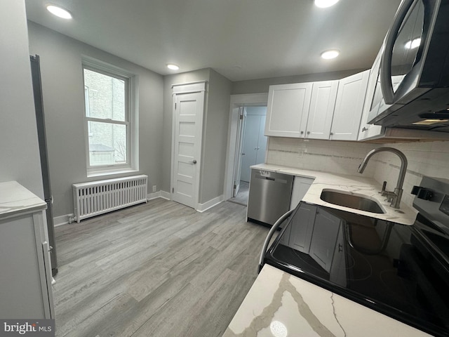 kitchen featuring sink, radiator heating unit, light hardwood / wood-style floors, white cabinets, and appliances with stainless steel finishes