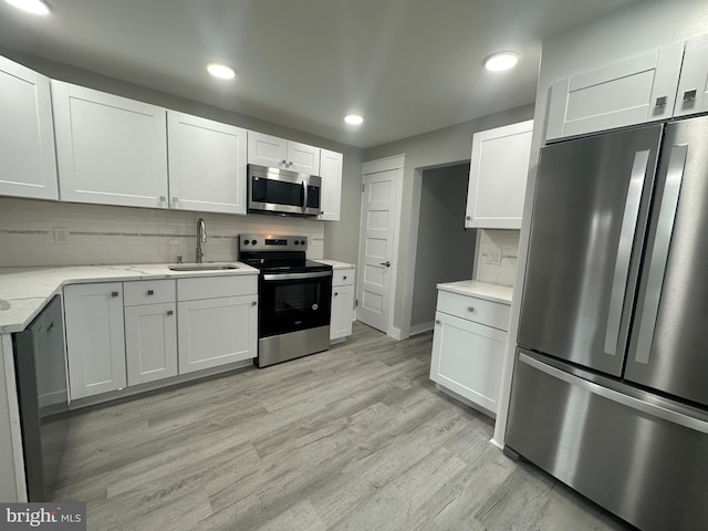 kitchen with sink, light wood-type flooring, appliances with stainless steel finishes, light stone counters, and white cabinetry