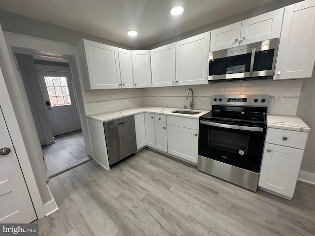 kitchen featuring sink, light hardwood / wood-style flooring, decorative backsplash, appliances with stainless steel finishes, and white cabinetry