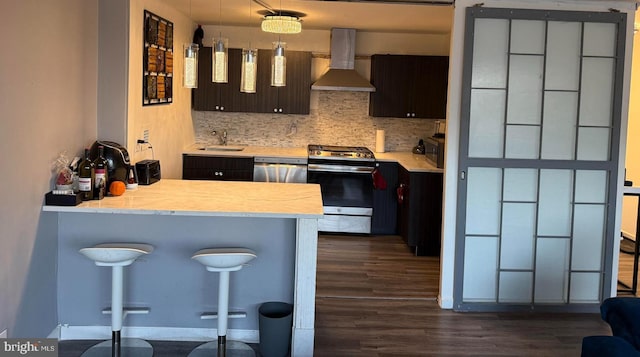 kitchen featuring dark brown cabinetry, wall chimney exhaust hood, stainless steel appliances, tasteful backsplash, and kitchen peninsula