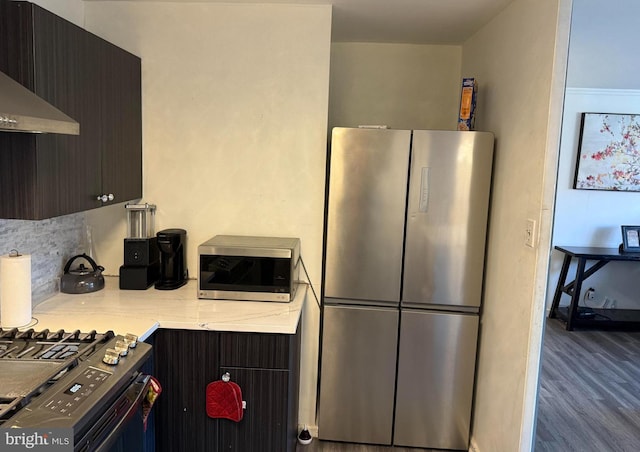 kitchen featuring stainless steel fridge, stove, dark brown cabinetry, dark hardwood / wood-style floors, and range hood