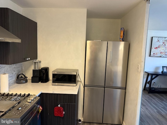 kitchen featuring hardwood / wood-style floors, stove, exhaust hood, dark brown cabinets, and stainless steel refrigerator