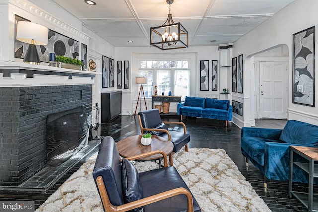 living room featuring dark hardwood / wood-style flooring, a chandelier, coffered ceiling, and a brick fireplace