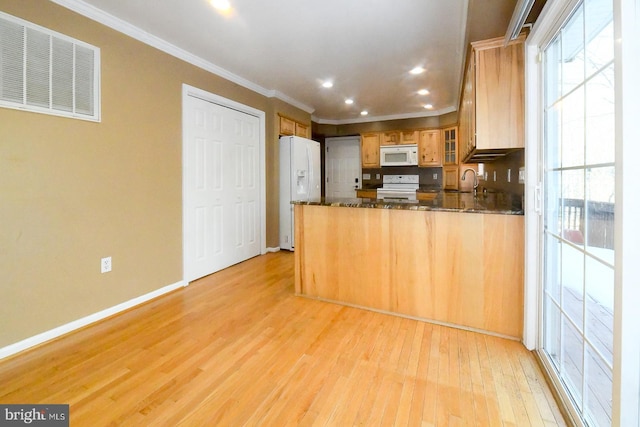 kitchen featuring white appliances, dark stone countertops, ornamental molding, kitchen peninsula, and light hardwood / wood-style flooring