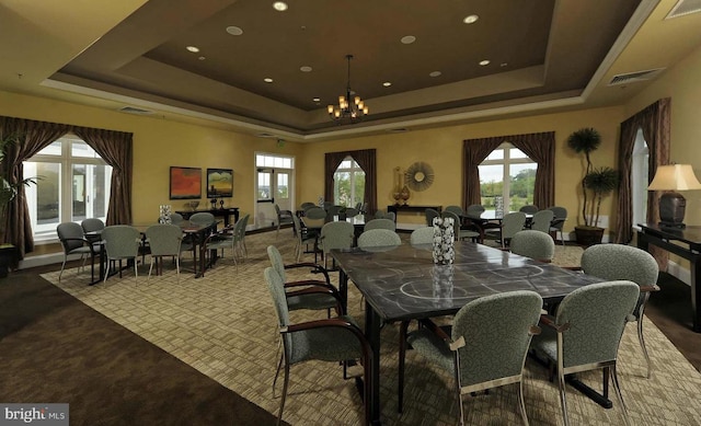 carpeted dining area with a chandelier and a tray ceiling