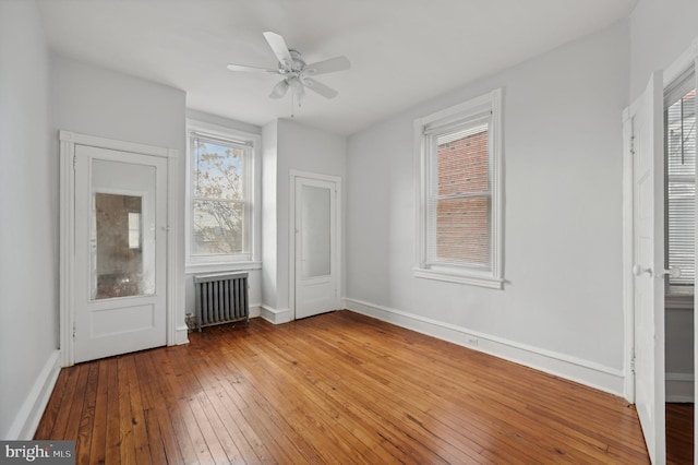 unfurnished bedroom with ceiling fan, light hardwood / wood-style floors, radiator heating unit, and multiple windows