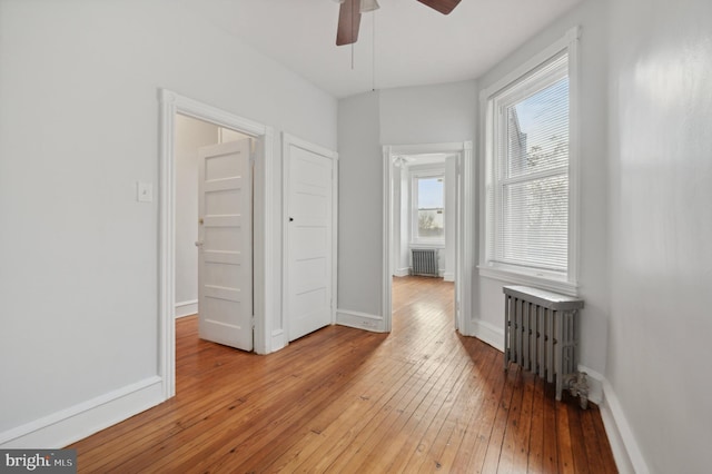 empty room featuring radiator, ceiling fan, and light wood-type flooring